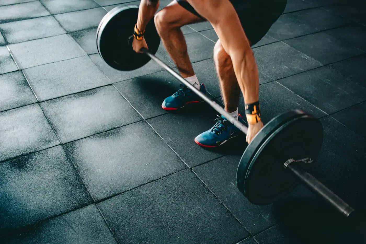 Loaded barbell resting on a dark gym floor, chalk on the knurling, lit from one side